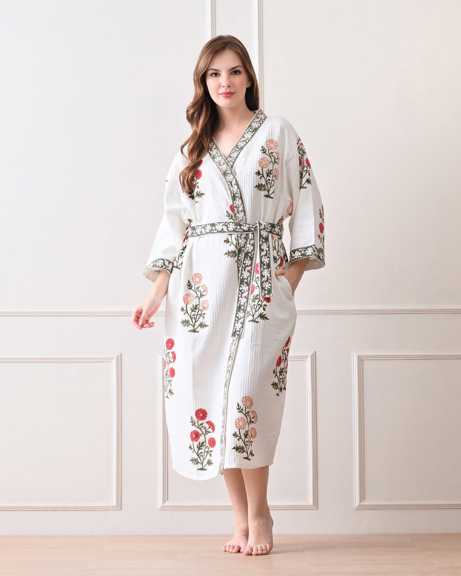 Meadow Light White Cotton Waffle Bathrobe with hand block printed floral patterns in red and orange, green leaves and green floral border, long sleeves, and waist tie belt, worn by a woman | Singhvis