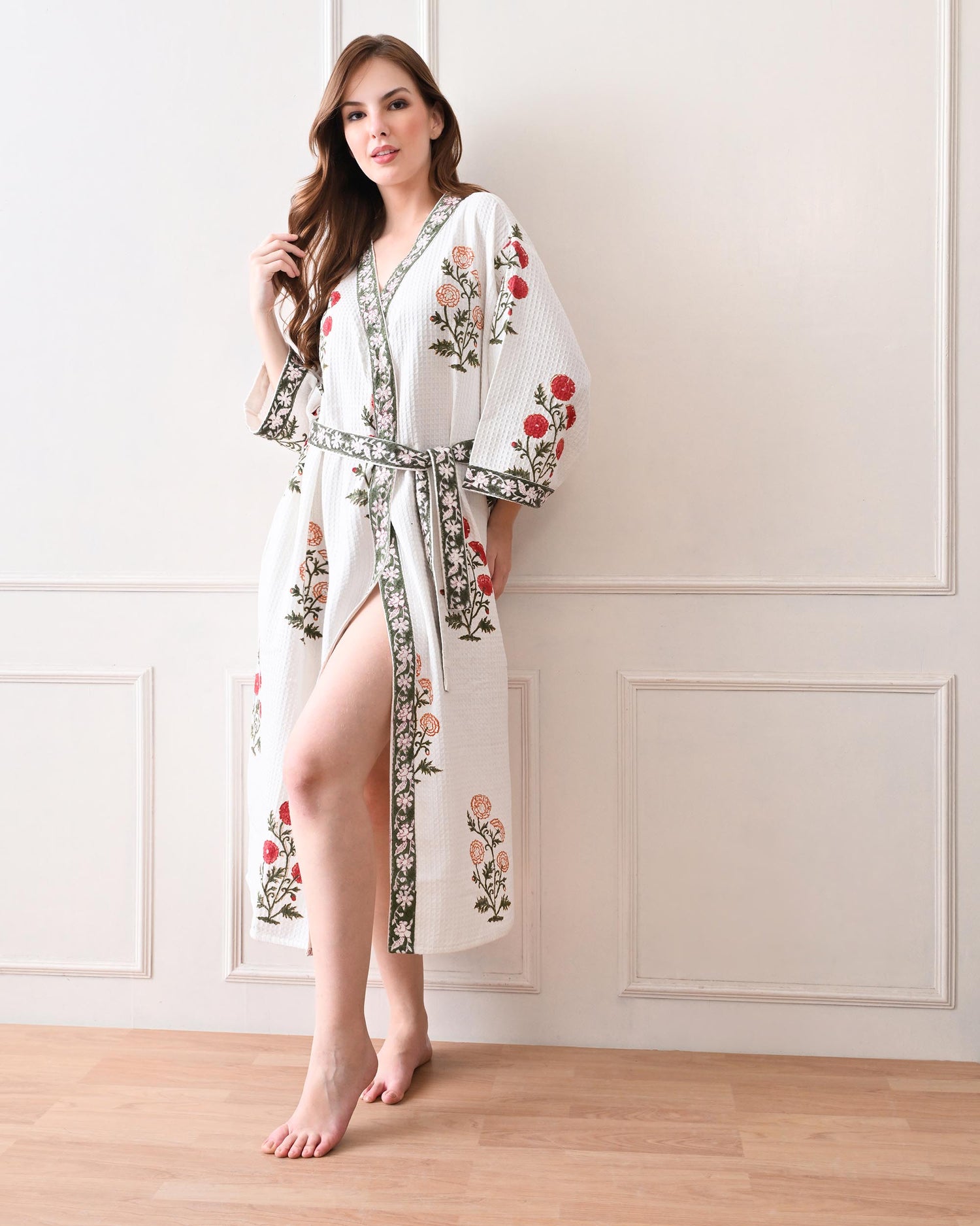Meadow Light White Cotton Waffle Bathrobe with hand block printed floral patterns in red and orange, green leaves and green floral border, long sleeves, and waist tie belt, worn by a woman | Singhvis