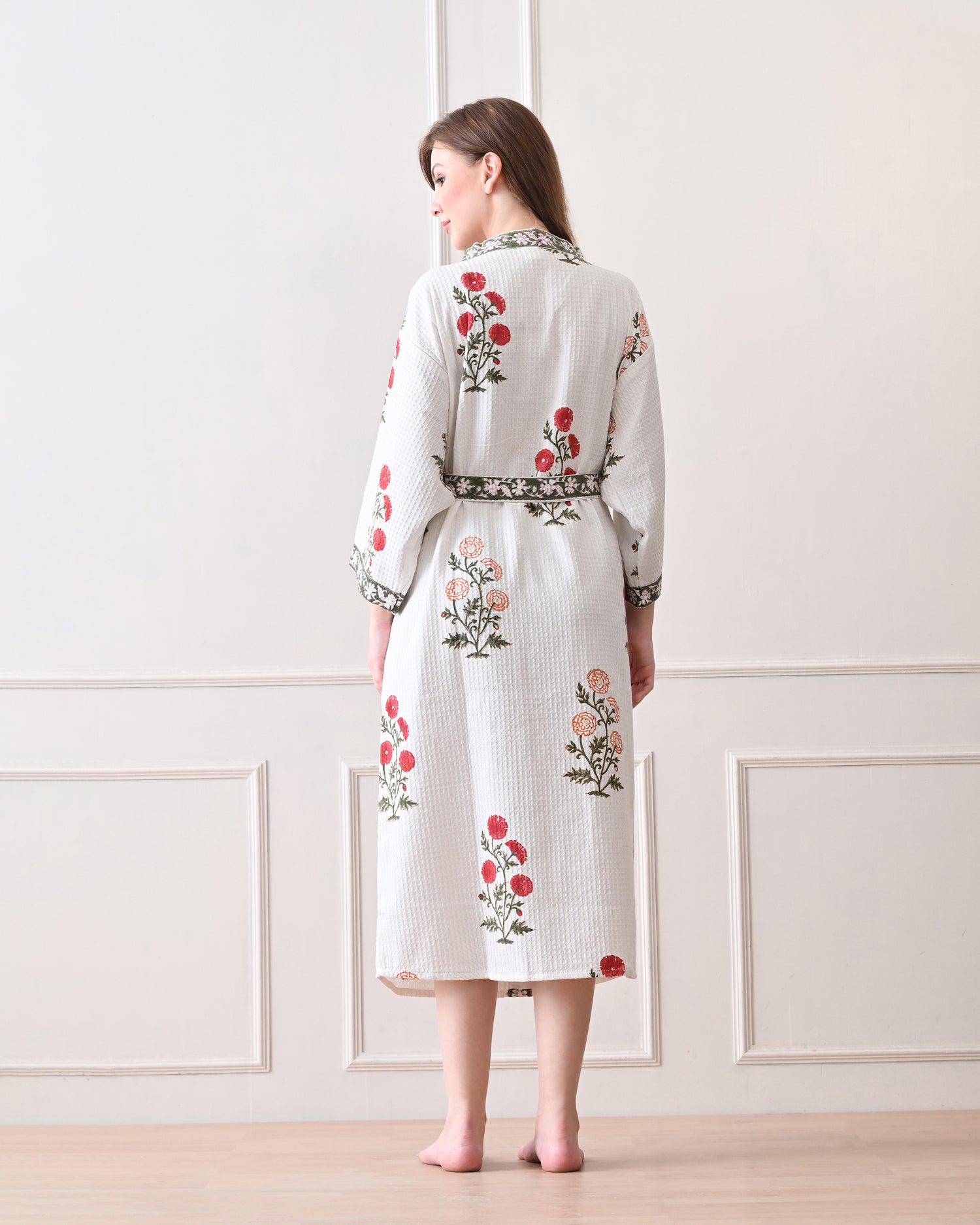 Meadow Light White Cotton Waffle Bathrobe with hand block printed floral patterns in red and orange, green leaves and green floral border, long sleeves, and waist tie belt, worn by a woman | Singhvis