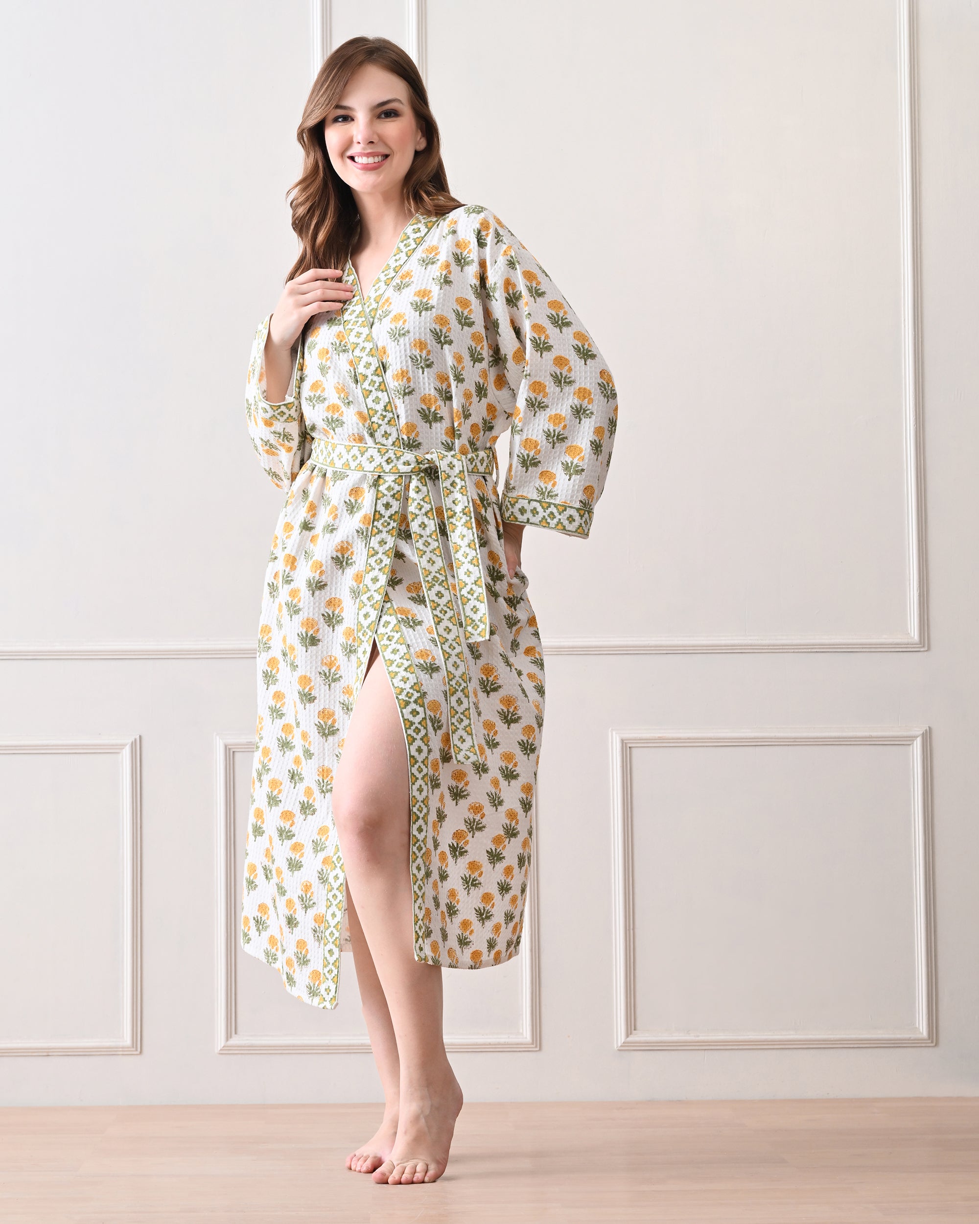 Sunrise Bloom Yellow Cotton Waffle Bathrobe with hand block printed yellow and orange flowers with green stems, green and white geometric border, long sleeves, and waist tie belt, worn by a woman | Singhvis