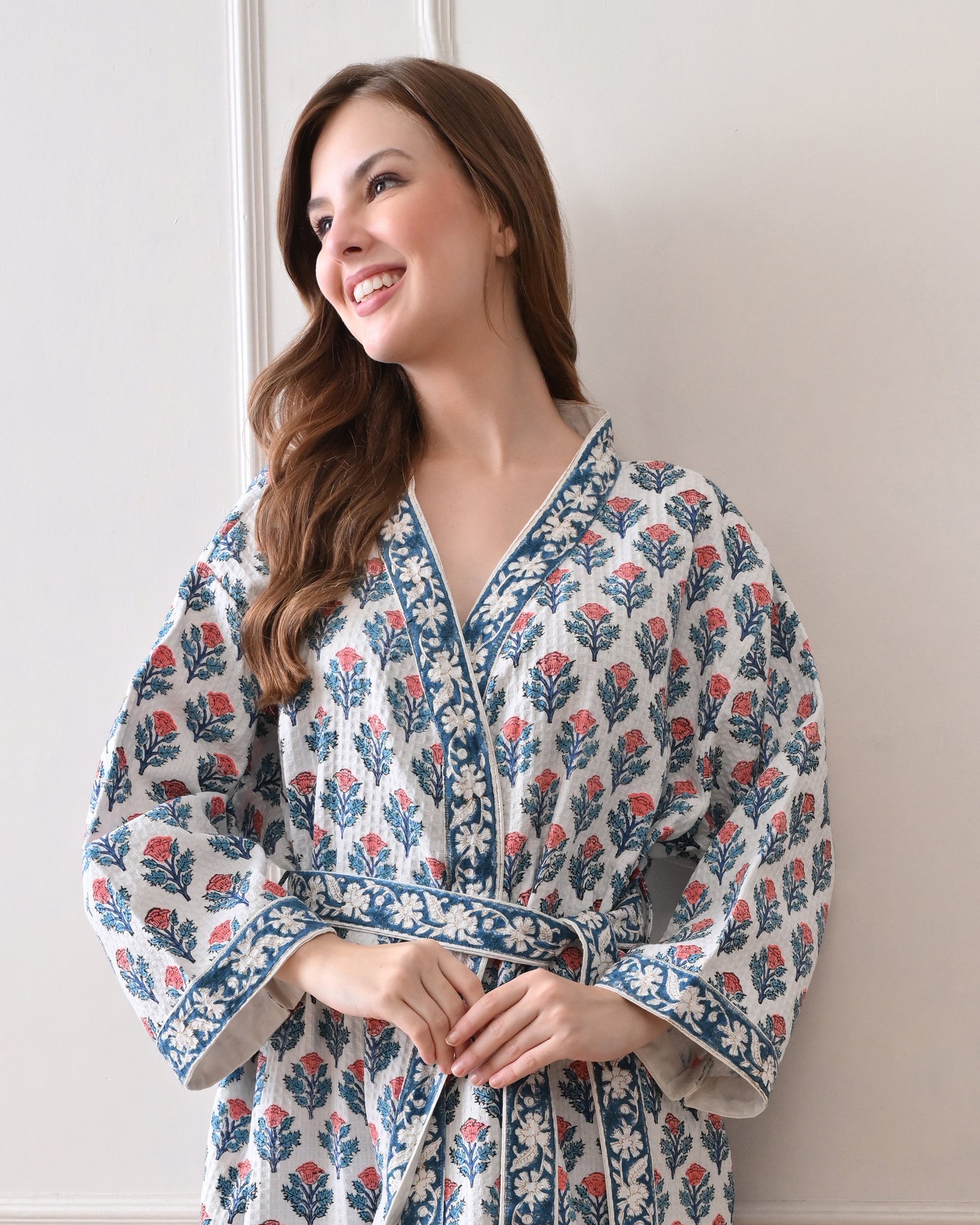 Tropic Blush Blue Cotton Waffle Bathrobe with hand block printed blue and pink floral patterns, blue floral border, long sleeves, and waist tie belt, worn by a woman | Singhvis
