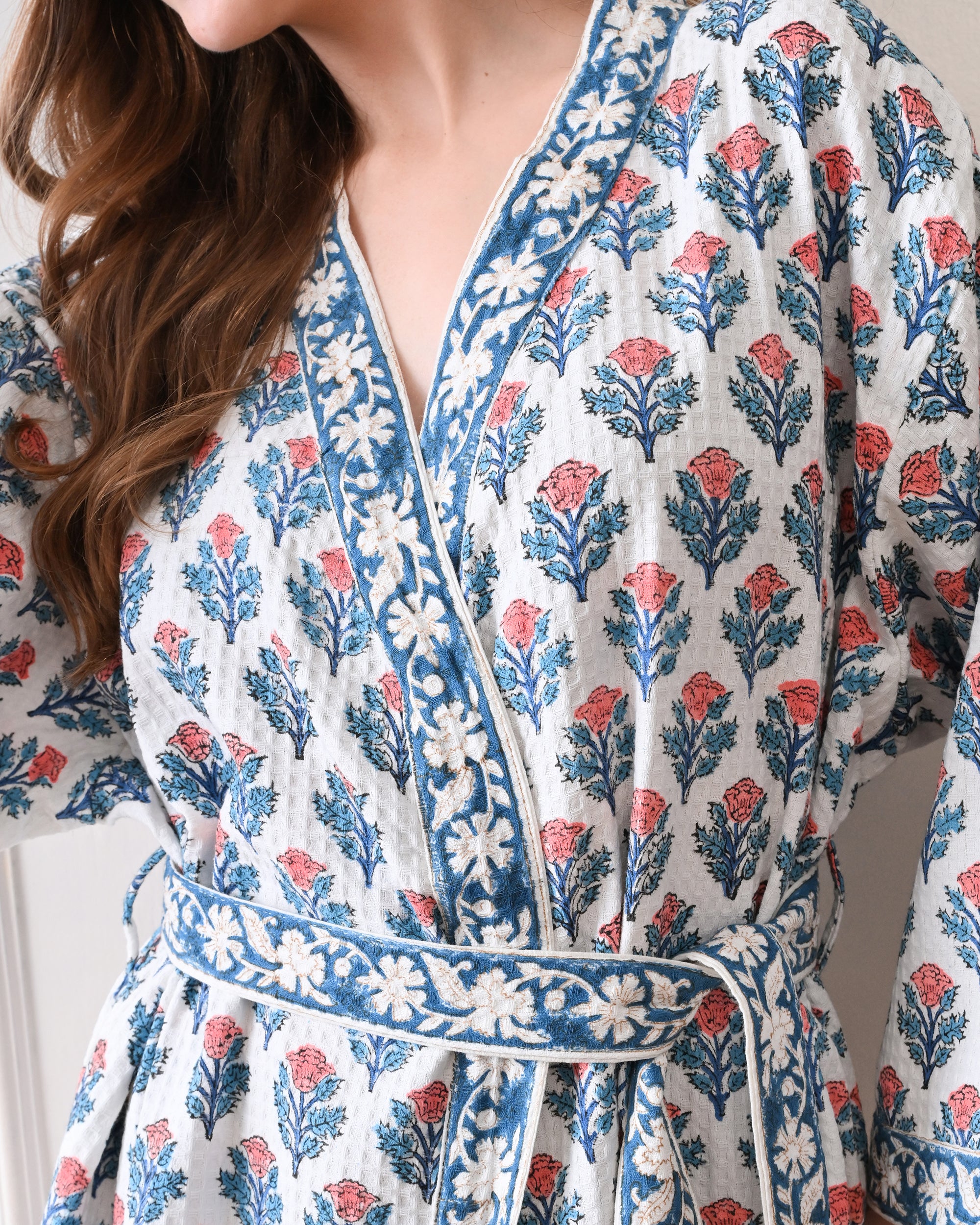 Tropic Blush Blue Cotton Waffle Bathrobe with hand block printed blue and pink floral patterns, blue floral border, long sleeves, and waist tie belt, worn by a woman | Singhvis