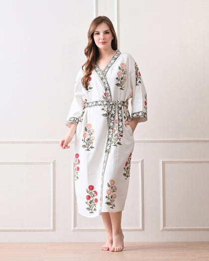 Meadow Light White Cotton Waffle Bathrobe with hand block printed floral patterns in red and orange, green leaves and green floral border, long sleeves, and waist tie belt, worn by a woman | Singhvis 