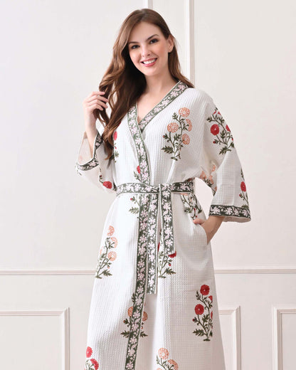 Meadow Light White Cotton Waffle Bathrobe with hand block printed floral patterns in red and orange, green leaves and green floral border, long sleeves, and waist tie belt, worn by a woman | Singhvis 