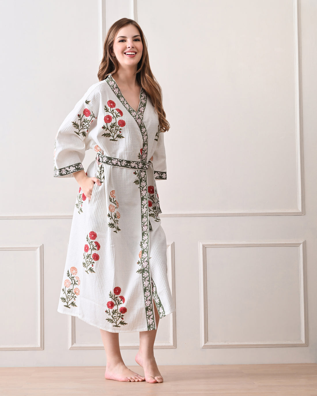 Meadow Light White Cotton Waffle Bathrobe with hand block printed floral patterns in red and orange, green leaves and green floral border, long sleeves, and waist tie belt, worn by a woman | Singhvis 