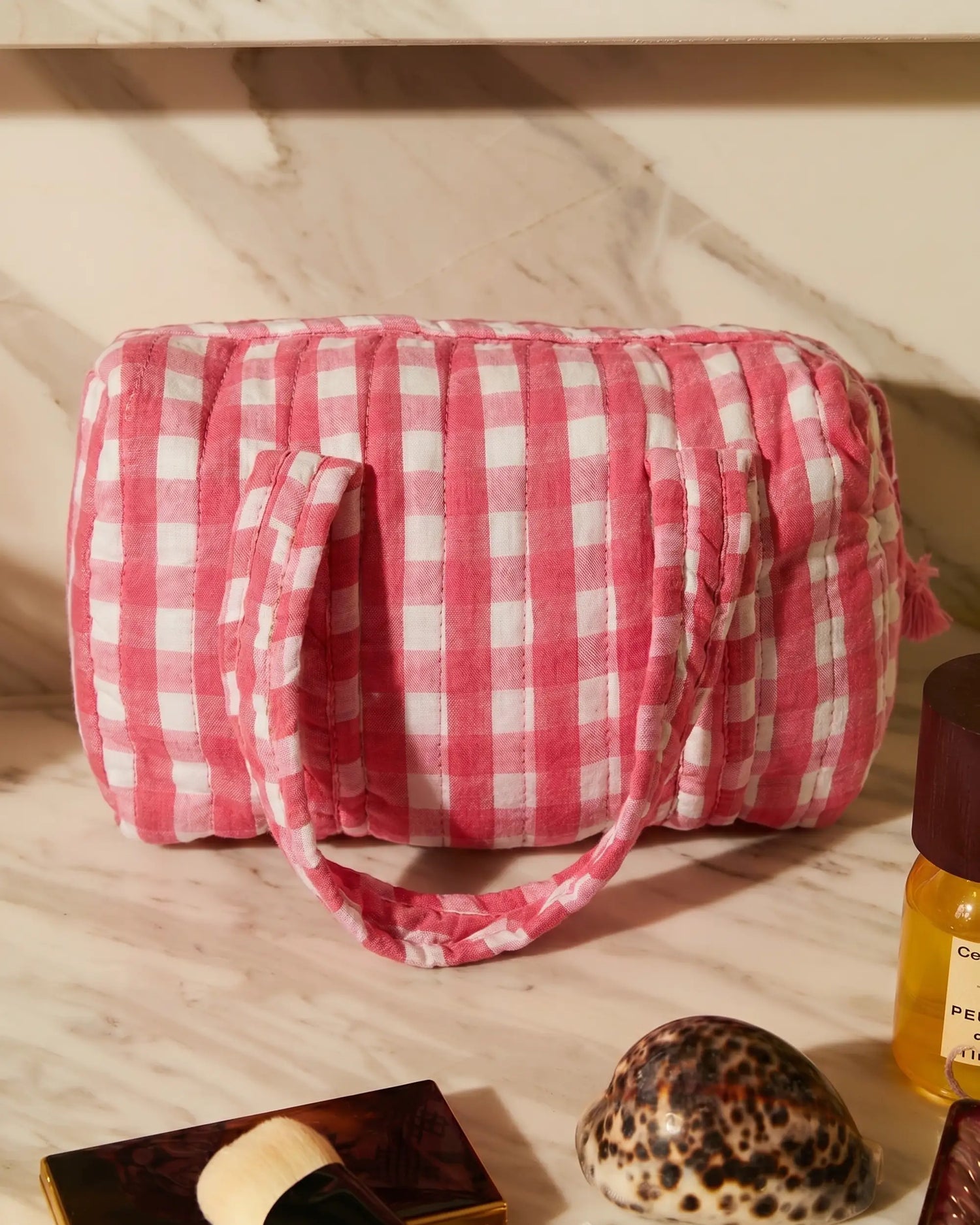 Pink gingham vanity bag with quilted finish and soft handles, placed on a marble countertop alongside beauty essentials | Singhvis