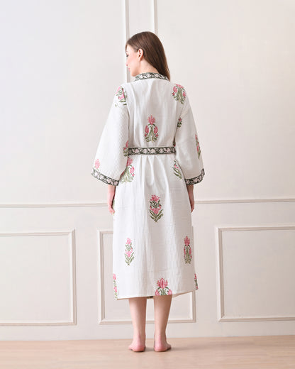 Botanic Whisper White Cotton Waffle Bathrobe with hand block printed pink tulip &amp; lotus-inspired floral patterns, green floral border, long sleeves, and waist tie belt, worn by a woman | Singhvis 