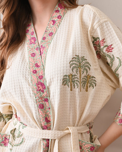  Island Flora White Cotton Waffle Bathrobe with hand block printed floral design, pink border, long sleeves, waist tie belt, worn by a woman | Singhvis