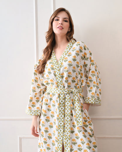 Sunrise Bloom Yellow Cotton Waffle Bathrobe with hand block printed yellow and orange flowers with green stems, green and white geometric border, long sleeves, and waist tie belt, worn by a woman | Singhvis