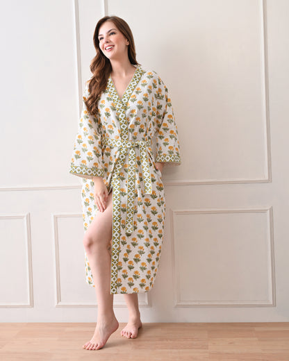 Sunrise Bloom Yellow Cotton Waffle Bathrobe with hand block printed yellow and orange flowers with green stems, green and white geometric border, long sleeves, and waist tie belt, worn by a woman | Singhvis